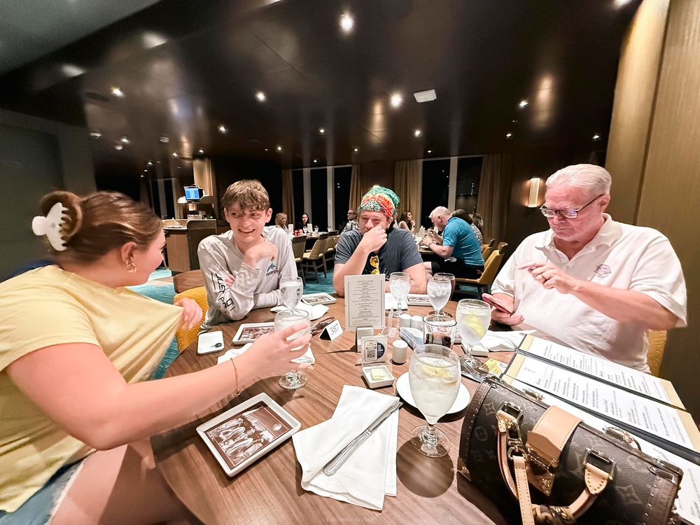 Family dining together at a restaurant table with drinks and menus in a warmly lit modern interior.