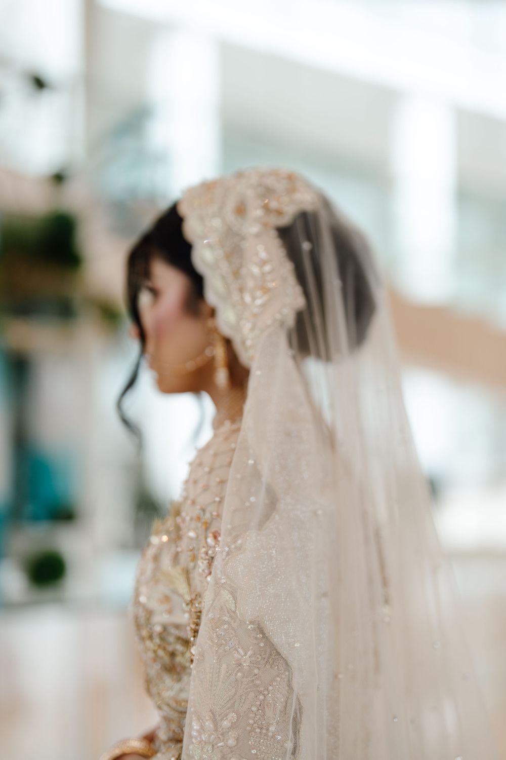 Close-up profile of South Asian bride wearing ornate beaded hijab veil and gold embroidered wedding dress.
