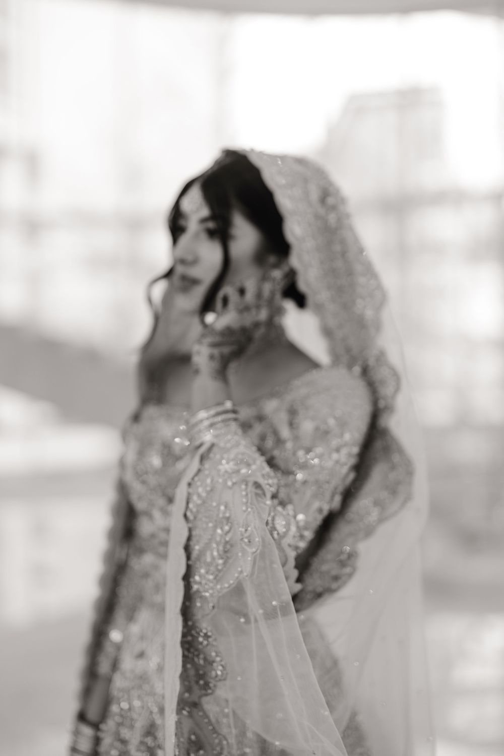 Black and white portrait of South Asian bride in heavily embroidered wedding gown and veil gazing downward.