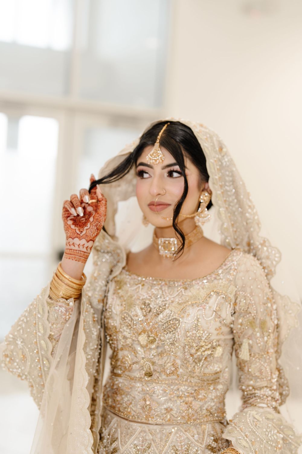 Elegant South Asian bride in gold embroidered bridal lehenga adjusting dupatta with henna-adorned hands.