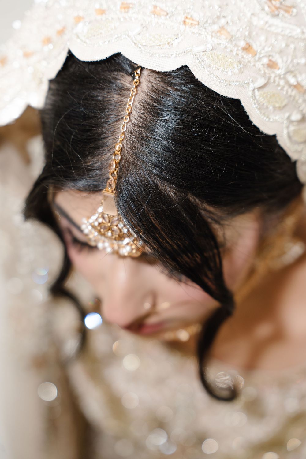 Close-up of South Asian bride with gold maang tikka hair jewelry and lace dupatta veil from above.