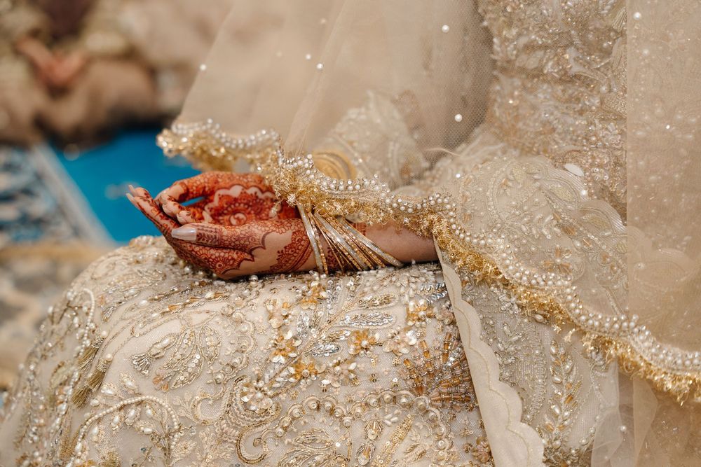 Close-up of bridal hands with red mehndi henna resting on gold embroidered ivory wedding lehenga.