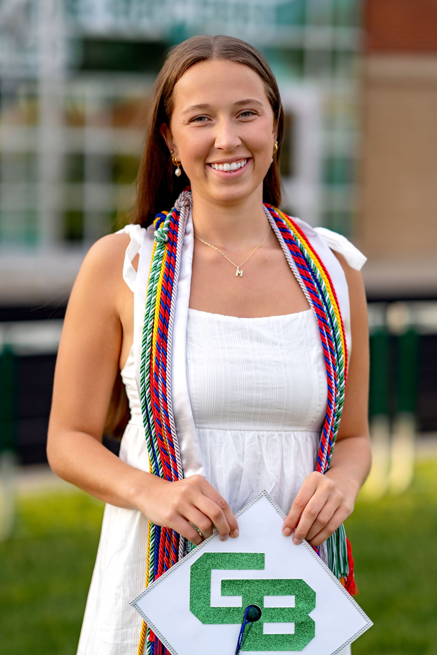 A person in a white dress holds up letters while wearing colorful rainbow suspenders in a graduation photo series.