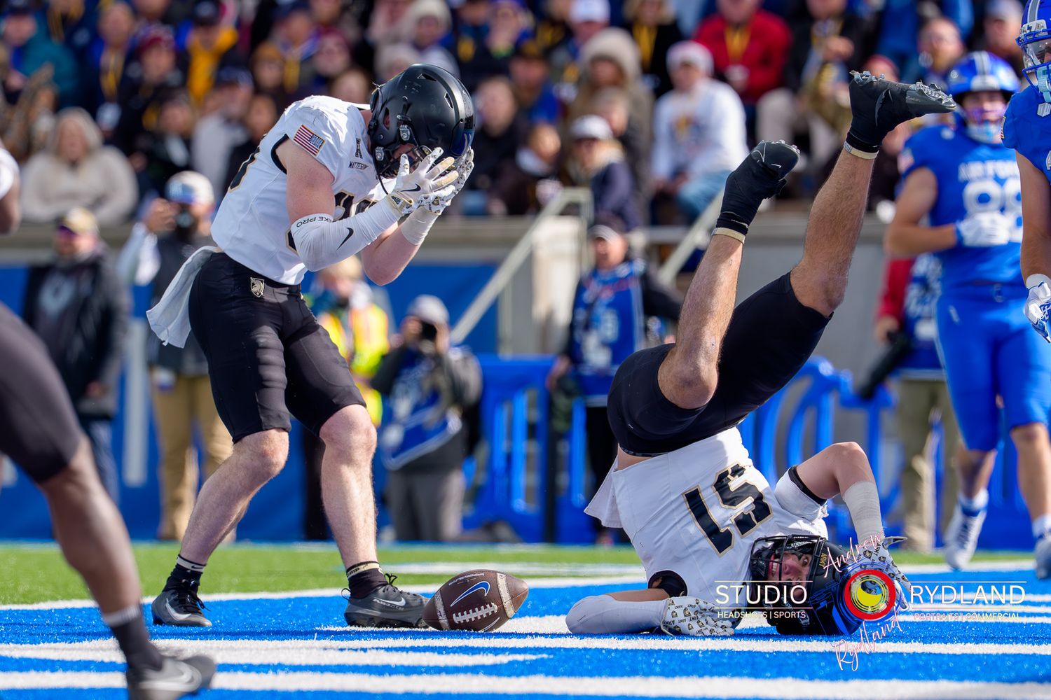 A football player tumbles and flips through the air during an intense play on the blue turf field.