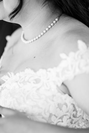 Black and white close-up portrait showing elegant pearl necklace and delicate lace details on wedding attire.