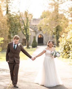 A couple holds hands and walks together on a sunny autumn day in their wedding attire.