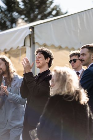 A group of people clapping and laughing together outdoors under a white tent canopy on a sunny day.