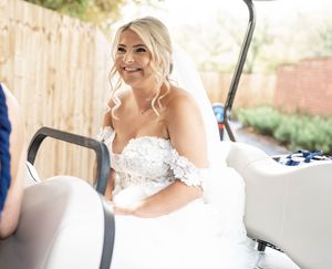 A bride in a white lace wedding dress smiles while getting ready for her wedding ceremony.