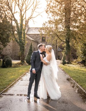 A couple shares a romantic moment on a wet stone path surrounded by autumn trees and fallen leaves.