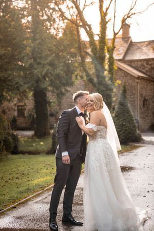 A couple shares a romantic moment on their wedding day outside a rustic stone building at sunset.