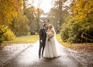 Wedding couple walks down tree-lined autumn path with golden foliage overhead.