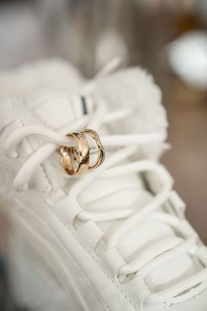 A pair of gold wedding rings resting on a white sneaker with laces, creating a unique wedding photography composition.