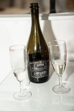 Empty wine glasses sit next to dark bottles on a white surface in a minimalist dining setup.