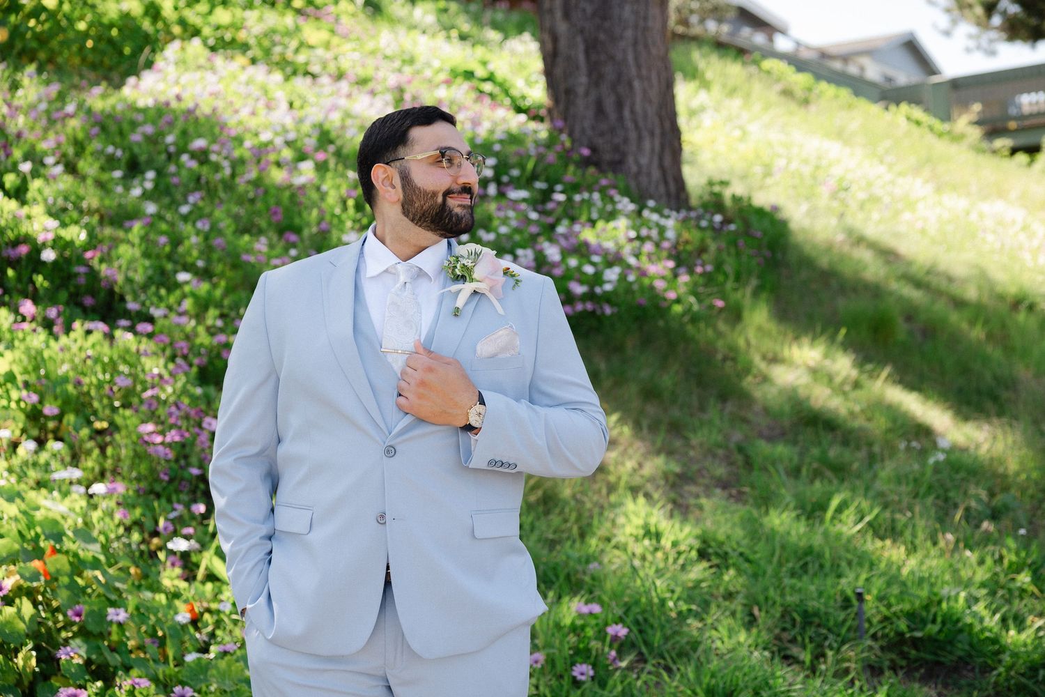 Elegant light blue wedding suit with white floral boutonniere, paisley tie and pocket square in garden setting.
