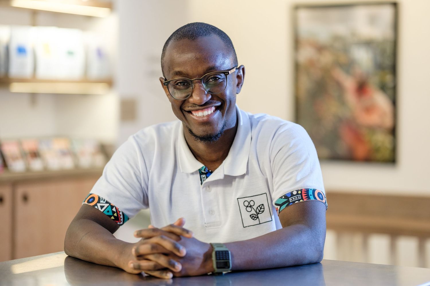 A person wearing a white polo shirt smiles while sitting at a table with a smartwatch on their wrist.