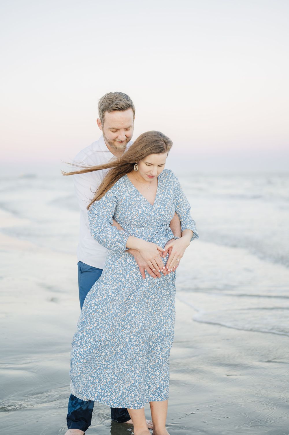 Playful couple in blue dress and white shirt share intimate moments along the shoreline at sunset.