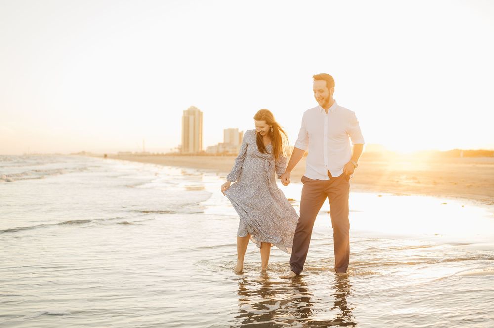 Couple holding hands walking along beach shore during golden sunset hour creating romantic silhouette.