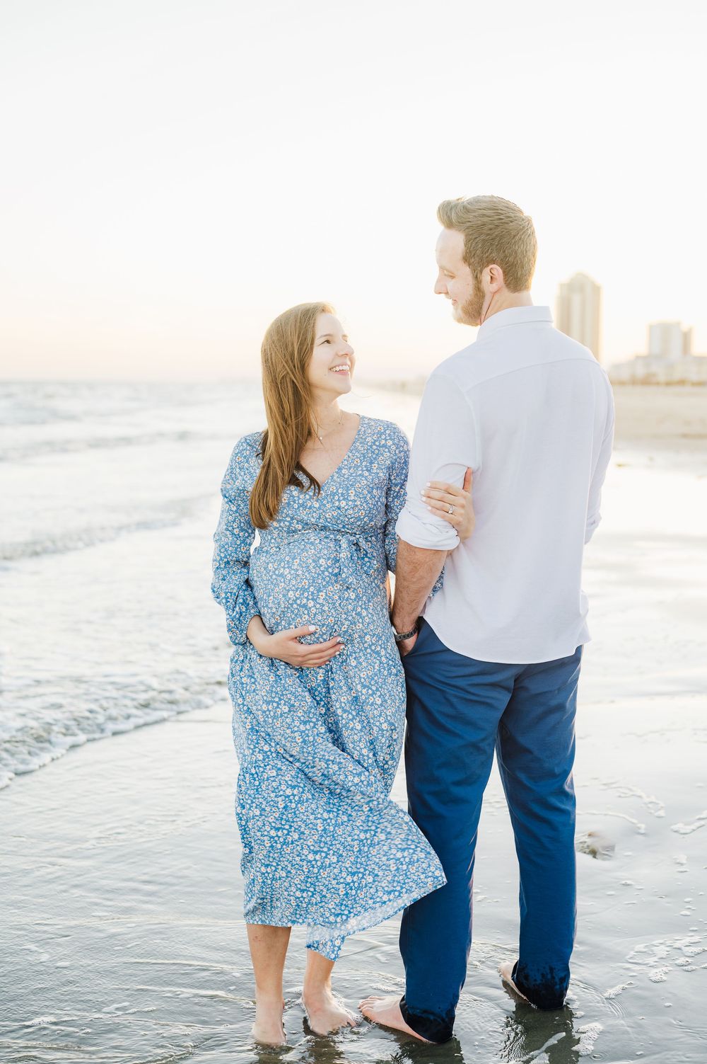 Couple walking together on a beach at sunset while wearing blue and white outfits.