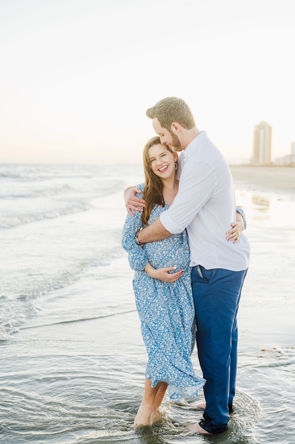 Romantic couple embraces on a sunny beach while waves lap at their feet in soft evening light.