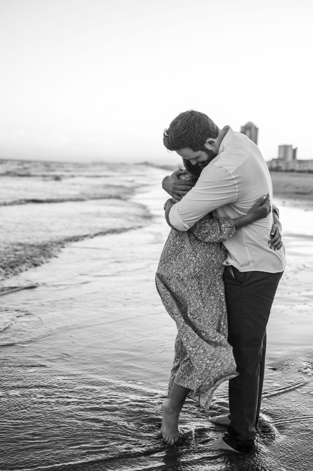 Romantic black and white photo of a couple embracing by the ocean waves.