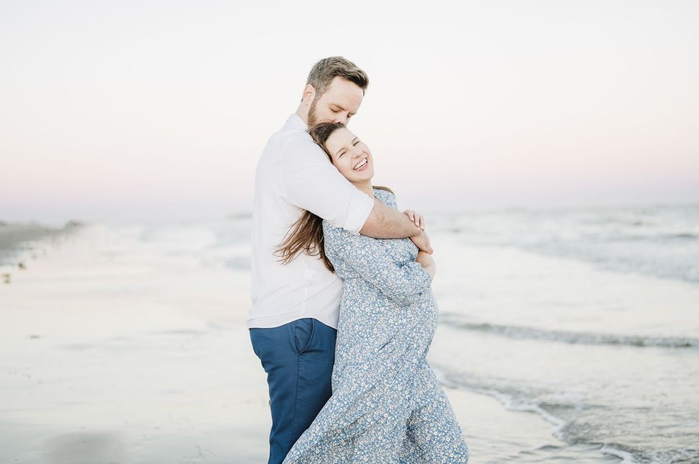 Romantic beach maternity photos with couple in coordinated blue and white outfits.