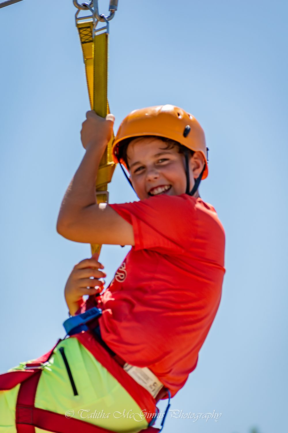 Someone in a red shirt and orange safety helmet enjoys an outdoor adventure activity against a blue sky background.