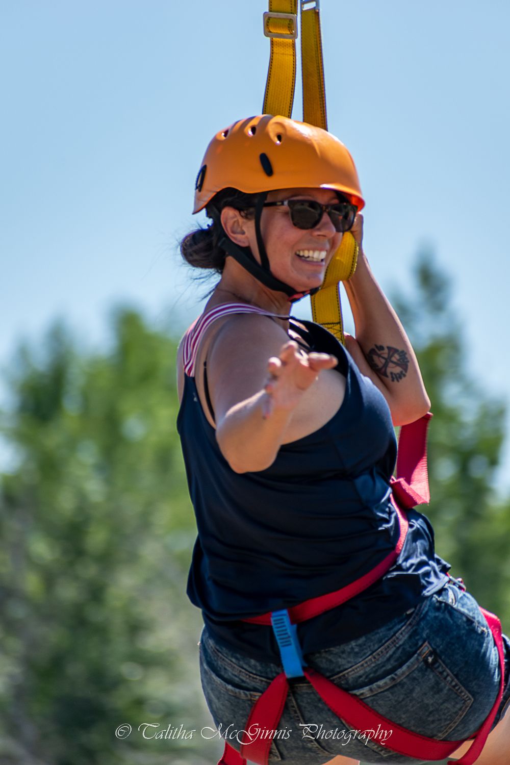Person in black shirt and orange helmet enjoying a zip line adventure through trees on a sunny day.