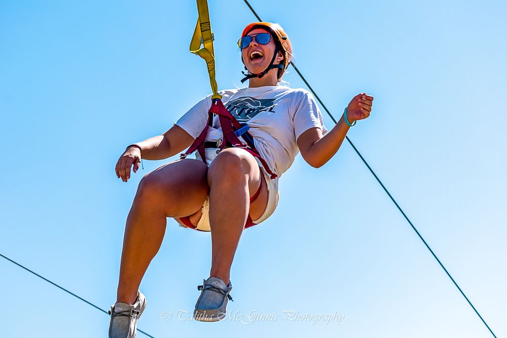 A person wearing a helmet and harness enjoys zip lining against a bright blue sky on a sunny day.