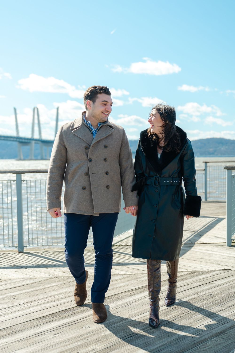 A couple walks together on a sunny boardwalk, sharing intimate moments against a bright blue sky backdrop.