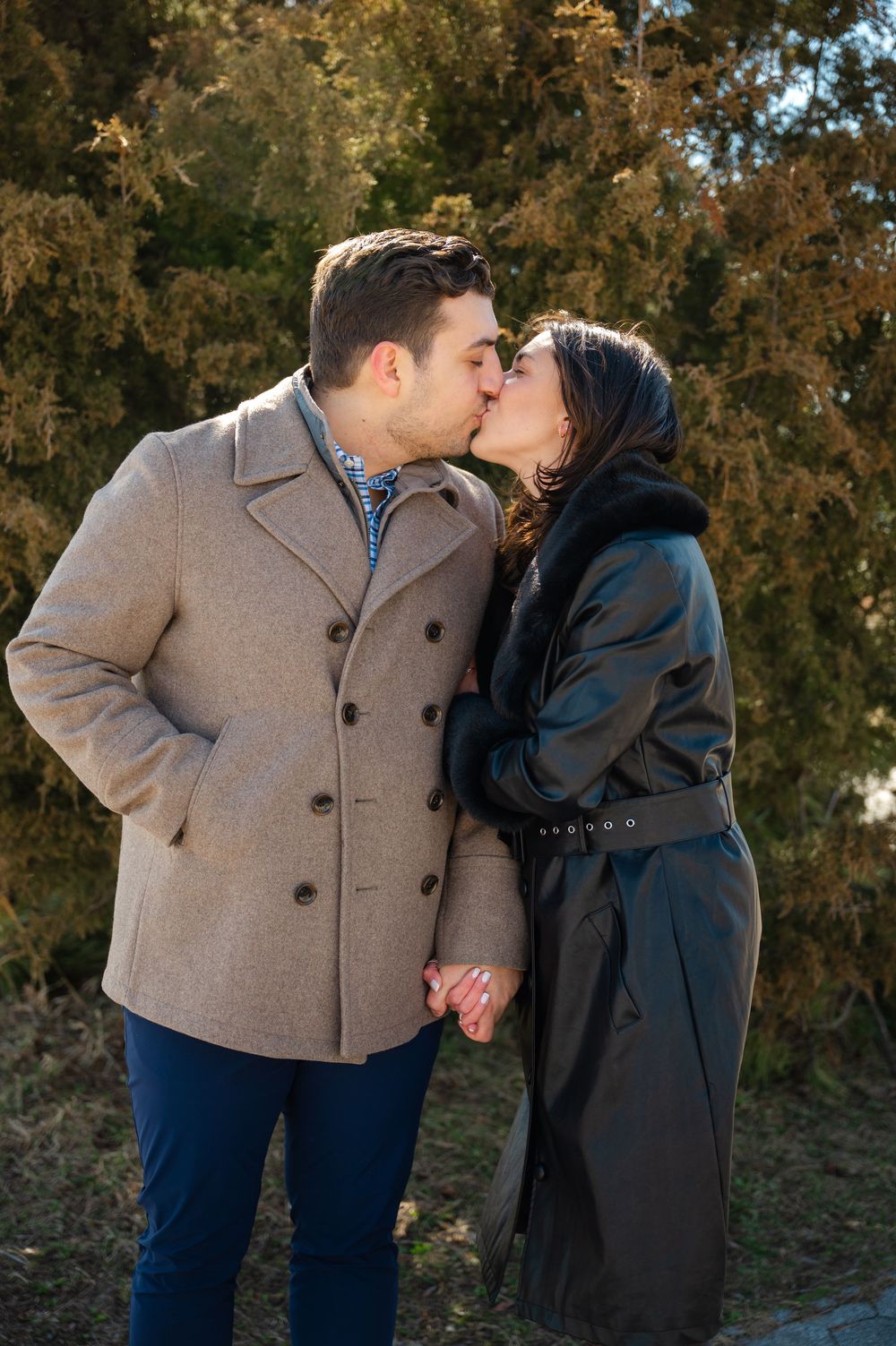 A couple in a grey coat and black coat share a romantic moment outdoors during autumn.