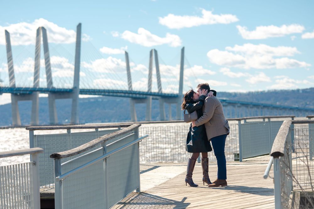 A romantic moment on a bridge deck overlooking water and mountains on a sunny day.