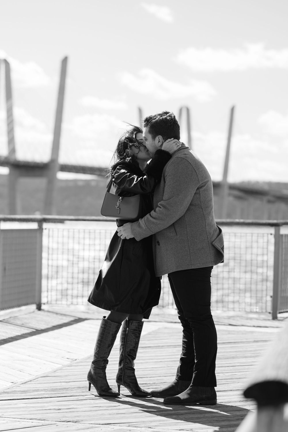 A romantic black and white photo of a couple sharing a tender moment on a wooden pier by the water.