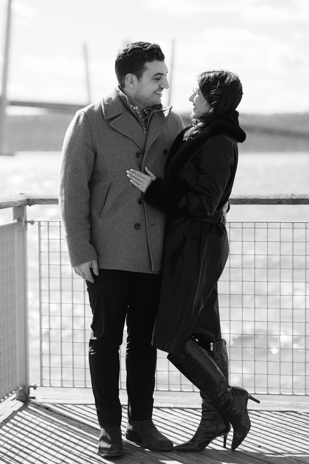 A couple embraces on a waterfront deck in black and white, creating an intimate monochromatic scene.