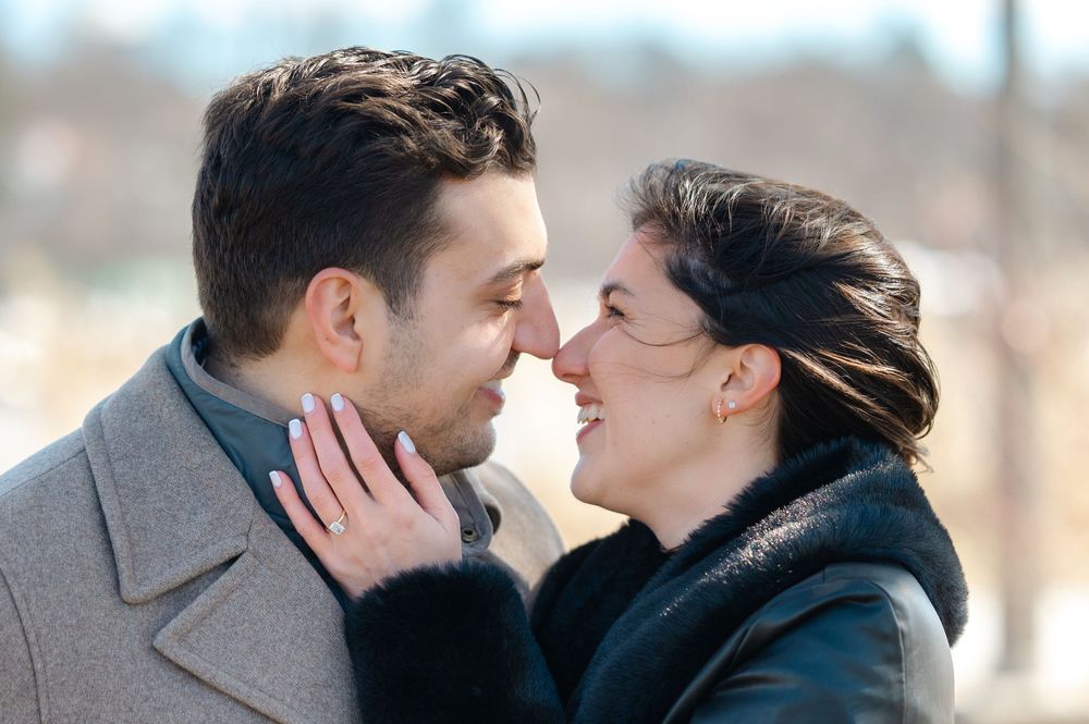 Romantic winter engagement photo shoot with couple in warm coats against snowy background.