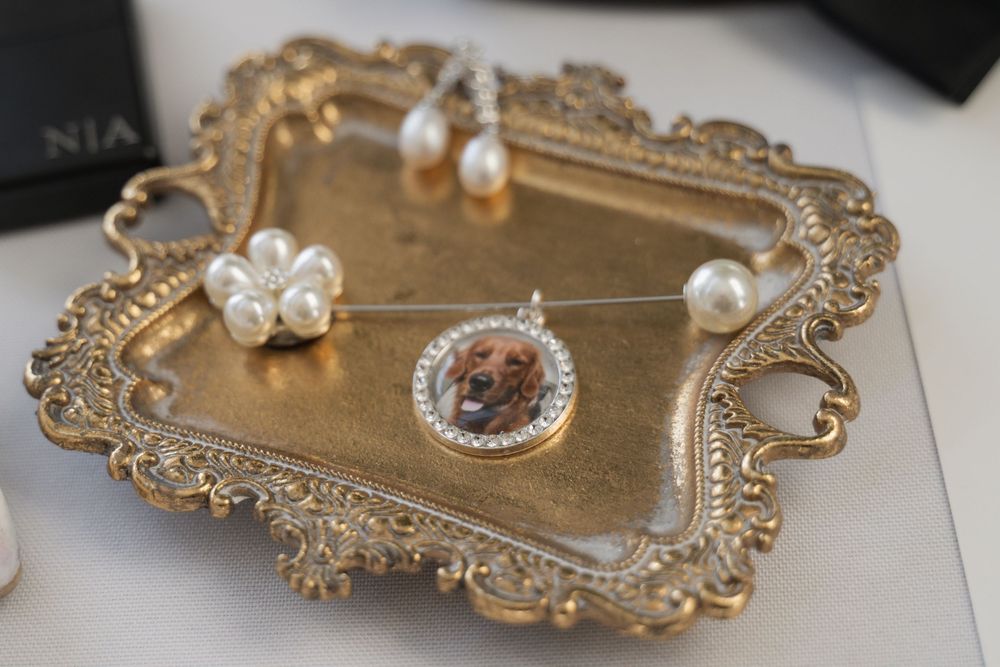 Gold ornate tray displaying pearl jewelry and a custom photo pendant necklace with rhinestone border.