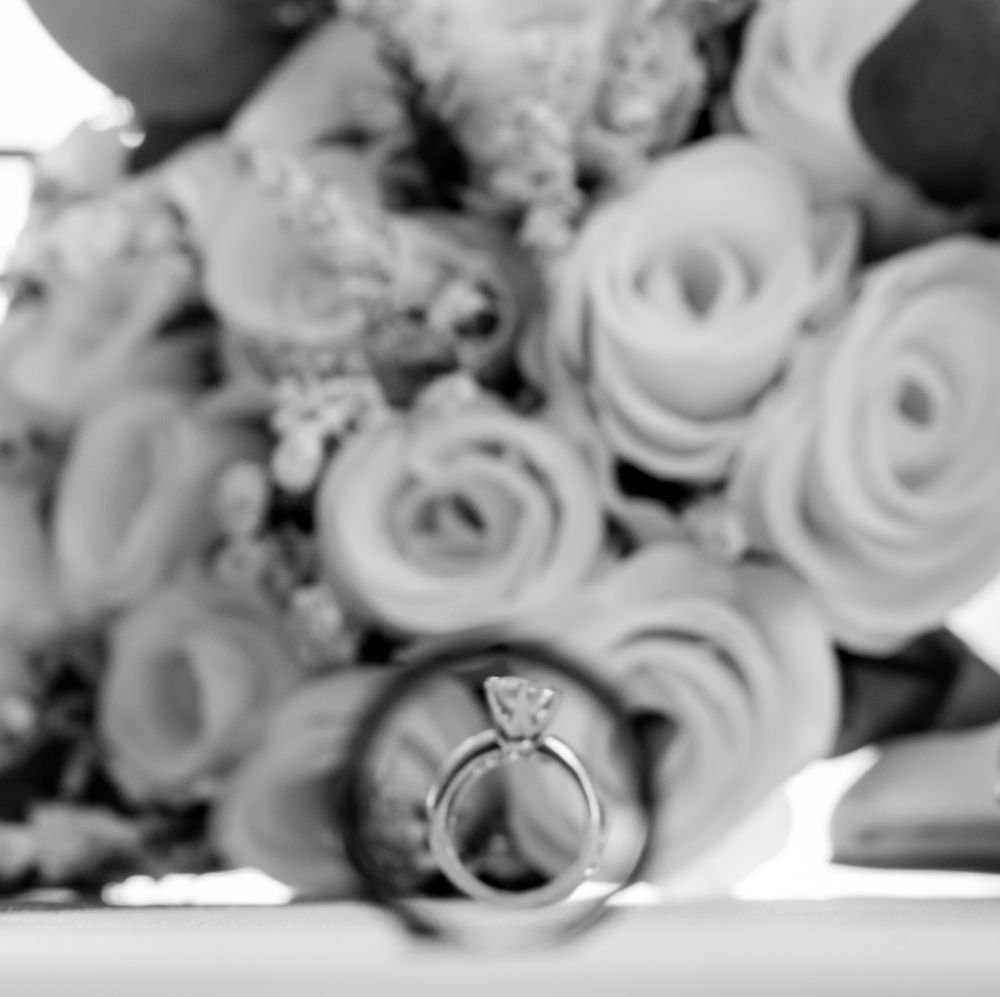 Black and white photo of diamond engagement ring and wedding band resting in front of a bouquet of roses.