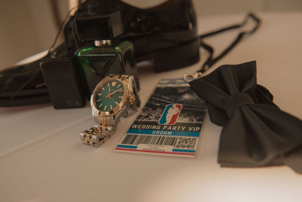 Groom wedding details flat lay featuring a green dial watch, bow tie, dress shoes, and VIP wedding party card.