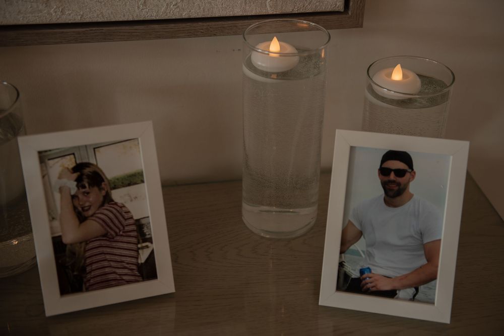 Two framed memorial photos flanked by glowing candles in glass holders on a table, honoring loved ones.