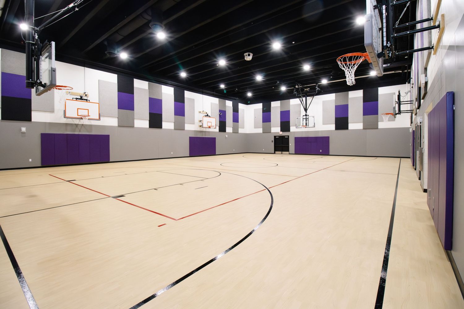 Dalhart Intermediate School gymnasium with hardwood floors, purple and gray wall panels, and multiple hoops under bright overhead lighting.