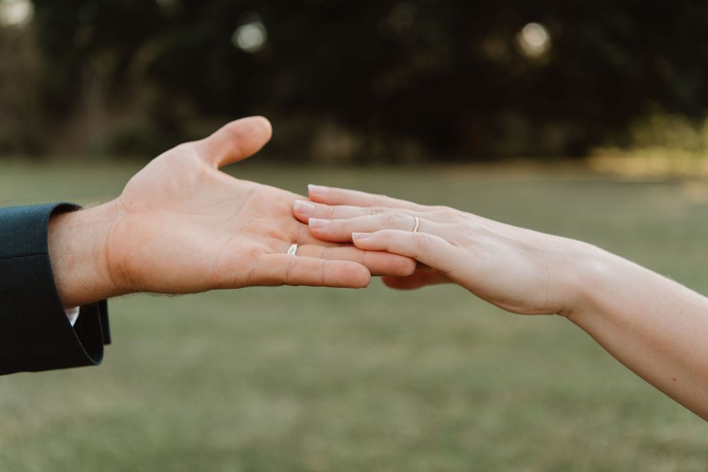 Close-up of two hands touching, with a gold wedding ring on the woman's finger, symbolizing marriage and love.