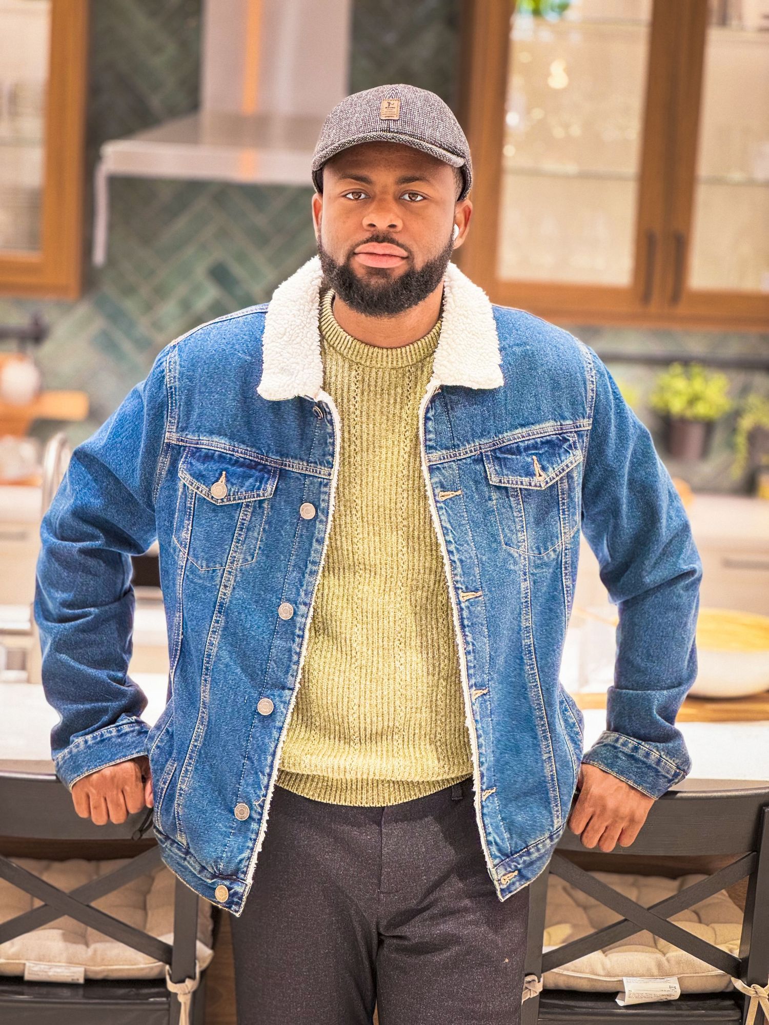 Casual portrait in denim jacket and yellow sweater against brick wall background.