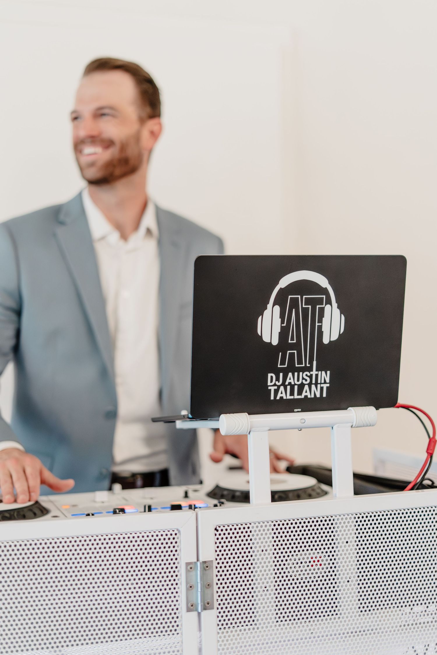 DJ Austin Tallant smiling behind a professional DJ setup with branded sign featuring headphones logo at an event.