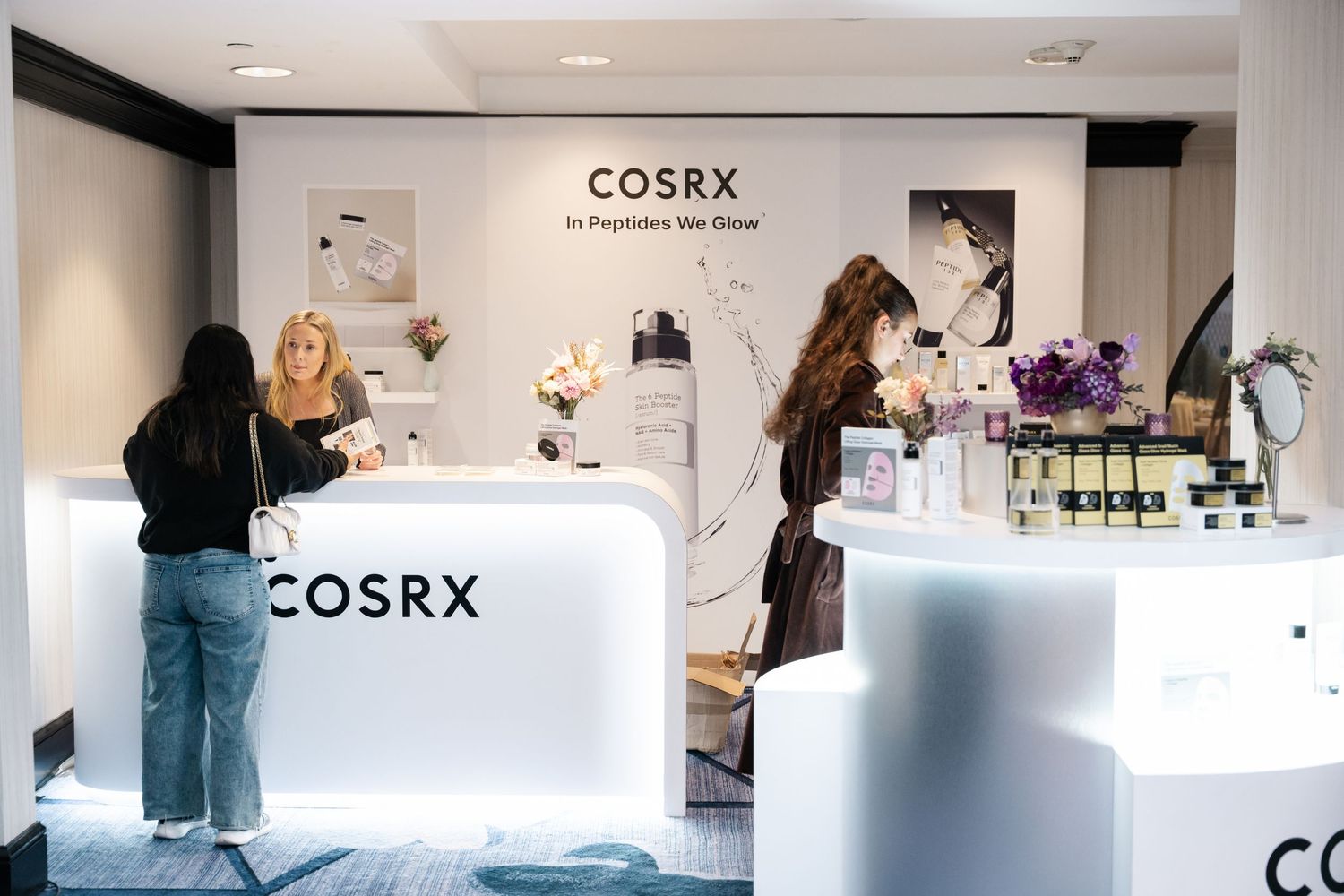 COSRX skincare pop-up store with illuminated white display counters and customers browsing products.