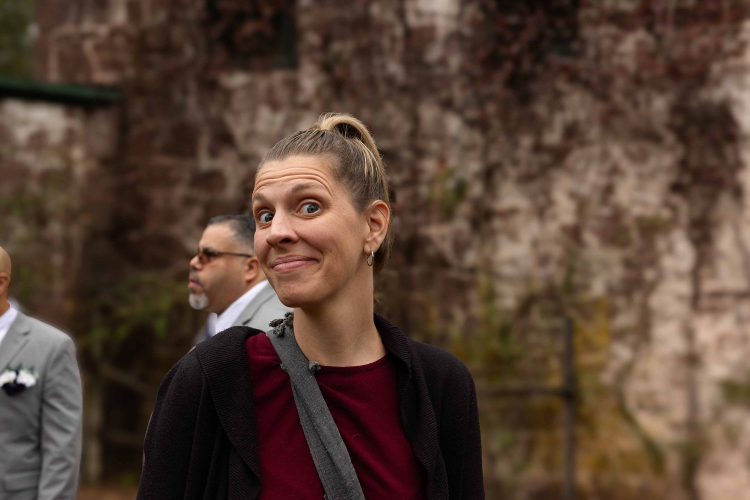 A group of people laughing and smiling while standing against a stone wall outdoors.