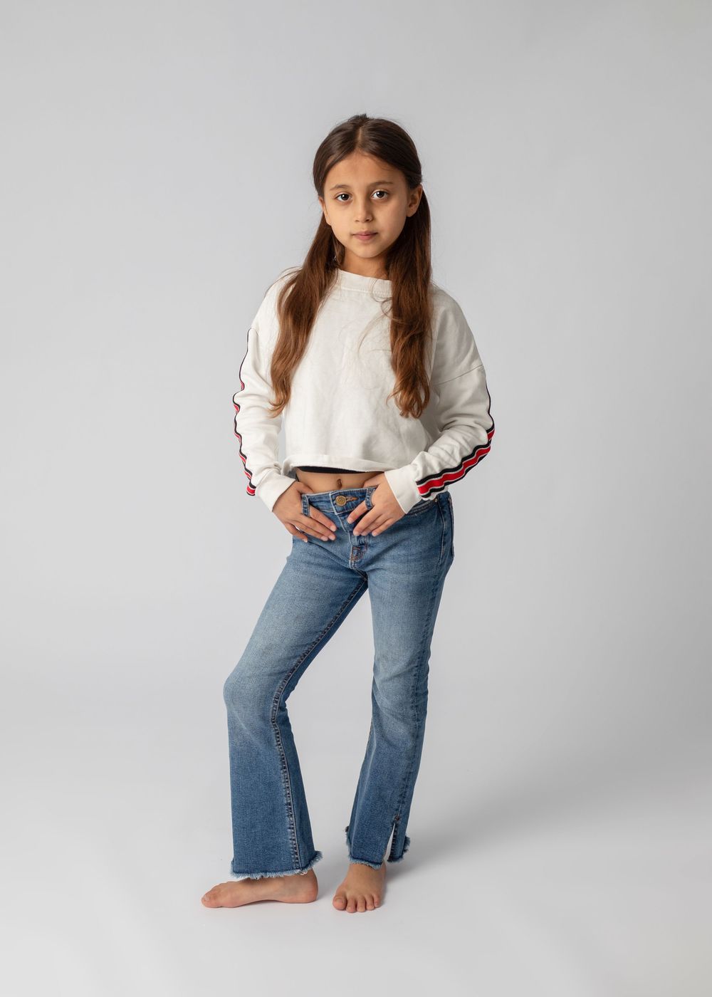 A young person in a white sweater and blue jeans poses in various casual stances against a light gray studio background.