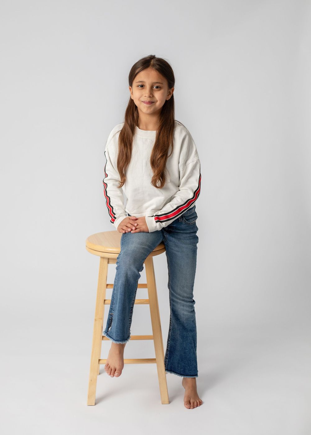 A person in blue jeans and white sweater sits on a wooden stool against a light gray background in four similar poses.