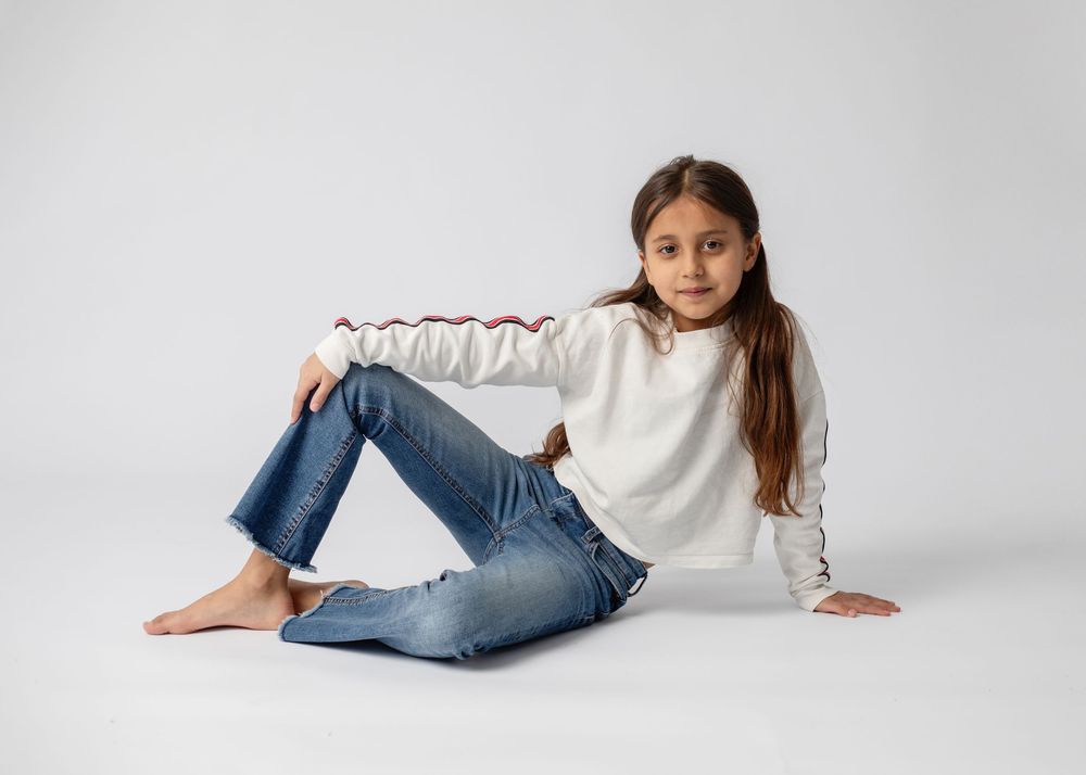 Person in casual white top and blue jeans posing in different relaxed positions against white studio background.