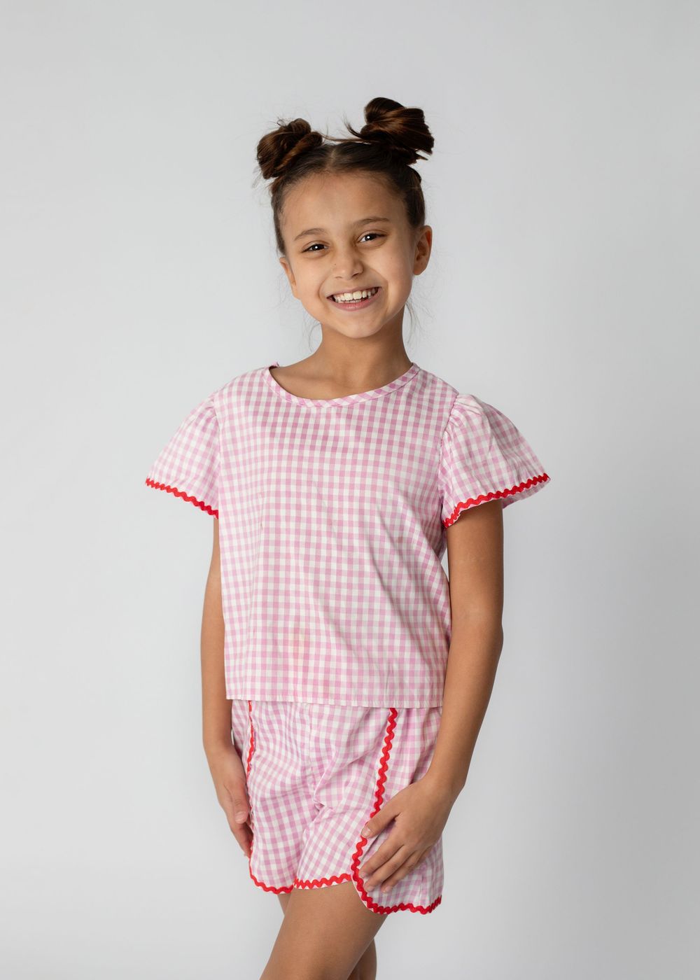 A child wearing a pink and white gingham dress with scalloped trim poses in four different playful stances.