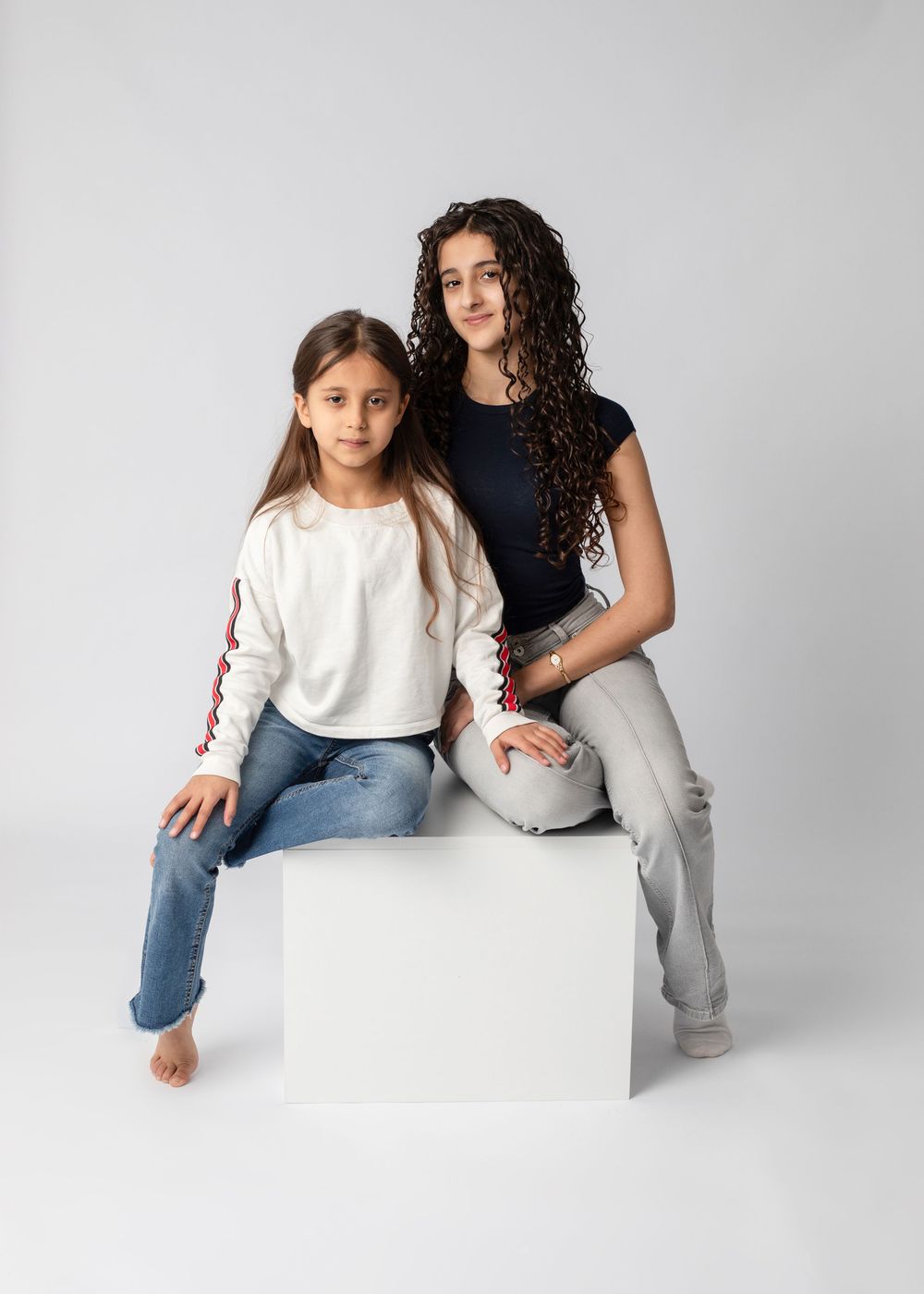 Three artistic studio photos show two people sitting and leaning on white blocks in casual denim and white outfits.