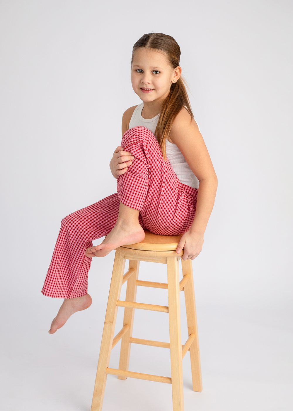 A child in a red and white polka dot dress sits and poses playfully on a wooden stool against a white backdrop.